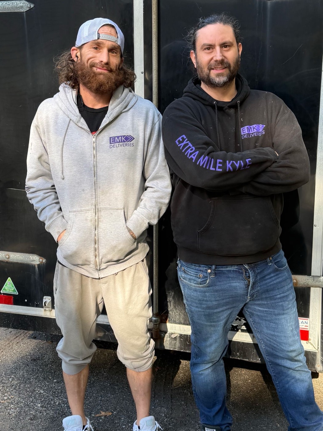 EMK Deliveries crew standing in front of the company trailer, one wearing an Extra Mile Kyle hoodie