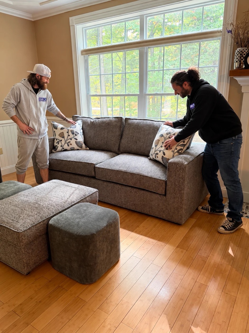 Two EMK Deliveries crew members styling pillows on a newly delivered sofa in a client's living room